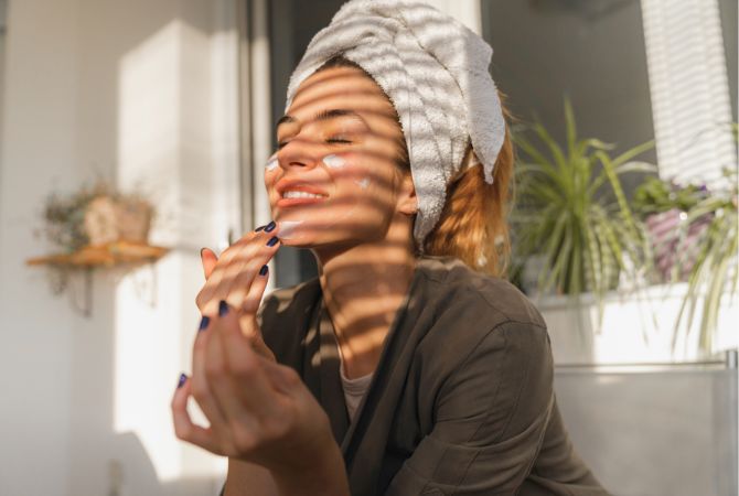 woman putting on skin care products in front of sun coming through window blinds